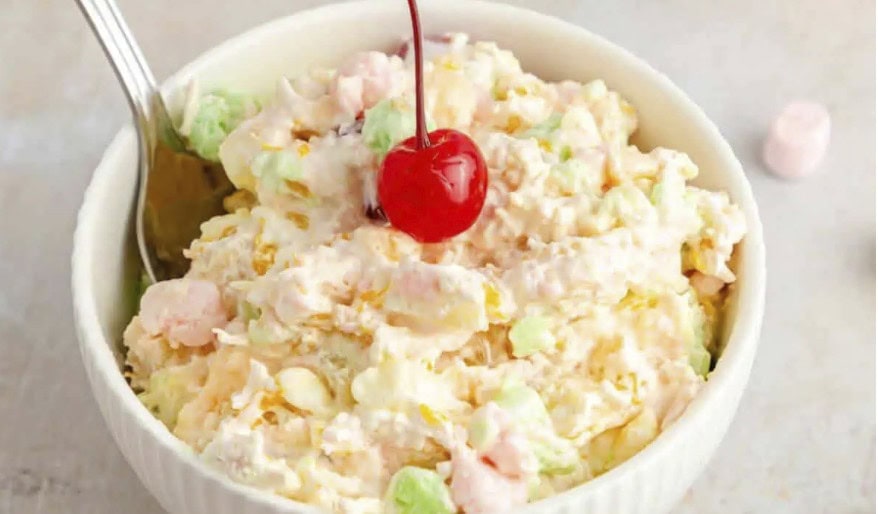 A bowl of creamy fruit salad with mini marshmallows, topped with a single maraschino cherry and a spoon on the side—perfect for backyard barbecue gatherings or as one of your go-to flavor-packed recipes.